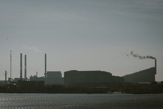 An atmospheric silhouette depicts a sprawling industrial landscape, complete with smokestacks and factories, highlighting the impact of industry on the environment.