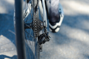 A close-up of a bicycle's rear wheel, showcasing the gears and chain, with a cyclist's foot partially visible, emphasizing cycling mechanics.