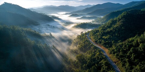 Road through mountain valley with mist and sunlight rays, aerial cinematic landscape, travel inspiration