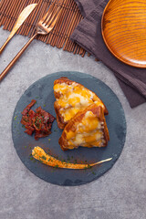 A gourmet dish with croissant halves topped with melted cheese, roasted vegetables, and creamy sauce, served on a slate plate.