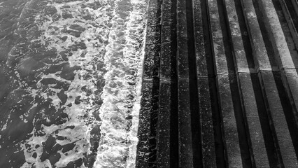 Black and white view of waves meeting a stepped concrete sea wall