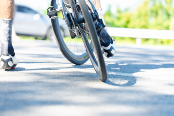 A cyclist's foot on a bike pedal, showcasing a flat tire on a sunlit road with a blurred car in the background.