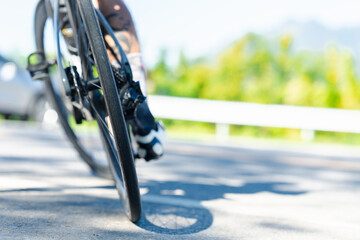 A cyclist's wheel in motion on a sunny road, capturing the essence of speed and outdoor activity against a blurred green background.