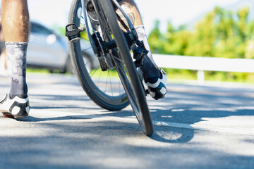 A cyclist is seen on the road, experiencing a flat tire, with a blurred background of greenery and a car parked nearby.