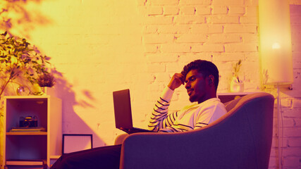 Man relaxing with laptop in cozy warm room. Concept of remote lifestyle, digital comfort, online study, flexible routine, peaceful work environment.