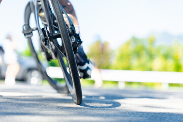 A close-up view of a bicycle wheel on a road, showcasing motion and the cyclist's leg, set against a blurred green background.