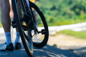 A cyclist's bike wheel on a winding road with greenery in the background, capturing a moment in outdoor cycling.