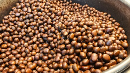 A close-up shot of a large pan filled to the brim with freshly roasted, shiny brown chestnuts, a popular seasonal street food snack.