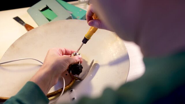 Man crafter repairing vintage electric lamp, using instruments and tools for disassembling light bulb socket, taking out screws with screwdriver. Renovating retro household items and upcycling hobby.