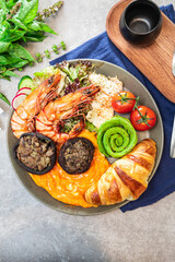 A brunch plate with grilled shrimp, scrambled eggs, croissant, avocado swirl, mushrooms, chicken, and salad.