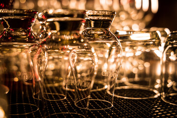 Upside-down glass cups on a rack with warm lighting and bokeh effect, creating a cozy bar ambiance.