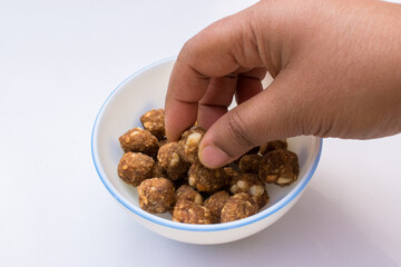 hand taking homemade mini jaggery balls or gud laddu served in a white bowl, representing a natural and healthy alternative to refined sugar