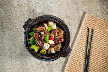 A stir-fry dish of beef short ribs with bell peppers and onions in a savory sauce, served in a black bowl.