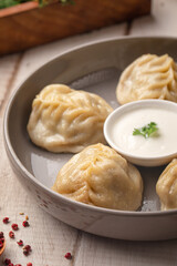Steamed manty dumplings with meat filling served with creamy sauce on a rustic wooden table