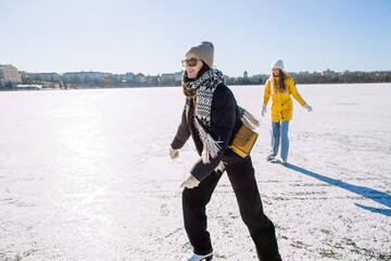 Young women ice skating on a frozen lake on sunny winter day