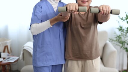 Asian senior elderly woman practice physiotherapy guided by caregiver nurse at home, holding dumbbells for rehabilitation exercise, mobility recovery improvement, muscle strength, healthcare wellness