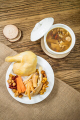 A traditional Chinese herbal chicken soup with goji berries, chicken feet, and medicinal roots, served in a bowl and plate on rustic tableware.