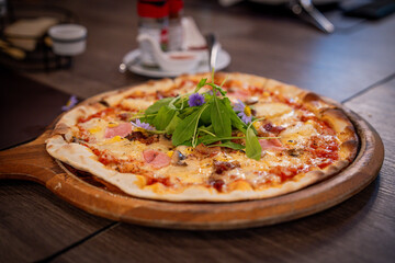 Baked gourmet pizza topped with melted cheese, ham, corn, and vibrant arugula with edible flowers. Served on a wooden board, the dish highlights warm colors, rich texture, and artisanal presentation.