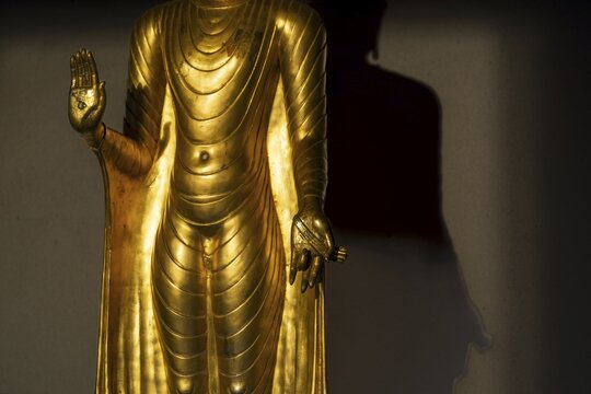Standing gilded Buddha statue, the right hand (raised, open palm facing outwards) symbolises the Abhaya mudra, the gesture of fearlessness, the left hand (opened downwards in front of the body), this posture is the Varada mudra, the gesture of giving or the gesture of charity, Wat Chana Songkhram, Phra Nakhon, Bangkok, Thailand