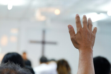 A believer raising a hand in prayer and worship during a church service. The soft focus and added film grain create a classic, emotional atmosphere. Ideal for themes of faith, worship, devotion