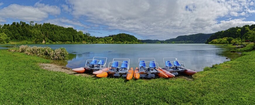 Tranquil Furnas Lake with pedal boats on the shore, surrounded by green nature and a cloudy sky, Furnas Lake, Furnas, Sao Miguel, Azores, Portugal