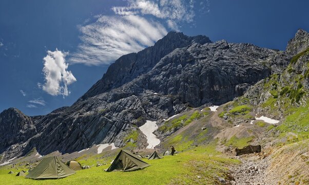 Tents of mountain hunters in the foreground with imposing mountain cliffs and blue sky with foehn clouds in the background, Alpspitze, Kreuzeck, Osterfelder Abfahrt, AlpspiX, Garmisch-Partenkirchen, Wetterstein range, Bavaria, Germany