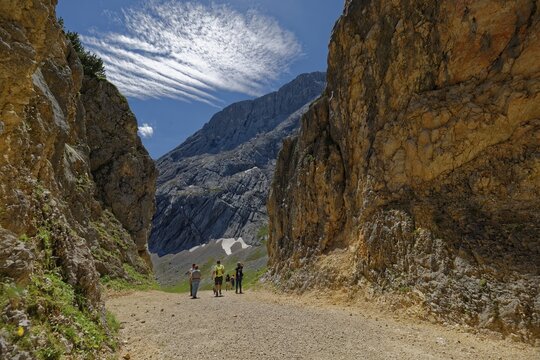 A group of hikers on a mountain path surrounded by imposing rocks under a blue sky with foehn clouds, rock breakthrough, Alpspitze, Kreuzeck, Osterfelderkopf, AlpspiX, Garmisch-Partenkirchen, Wetterstein range, Bavaria, Germany