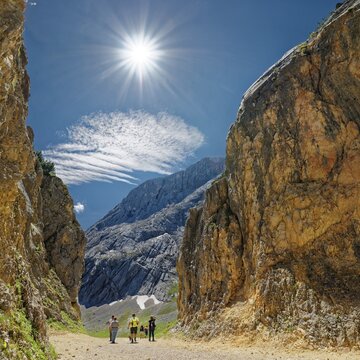 A group of hikers between imposing rock faces under a bright blue sky with the sun above, rockfall, Alpspitze, Kreuzeck, Osterfelderkopf, AlpspiX, Garmisch-Partenkirchen, Wetterstein range, Bavaria, Germany