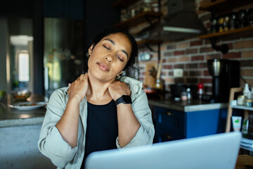 Adult woman tired, rubbing sore neck in home kitchen