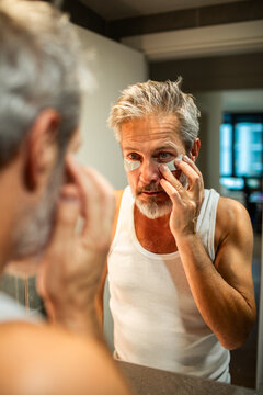 Mature man applying eye patches in home bathroom, focused
