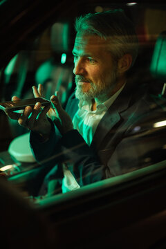 Mature man focused using voice assistant on phone in car at night