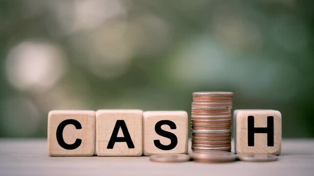 Wooden block with text Cash and stacks of coins against a blurred background.
