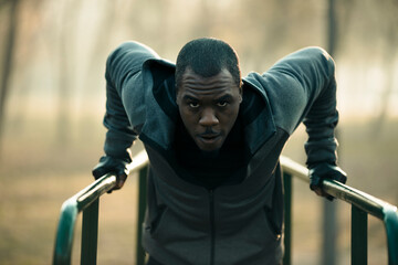 Determined young adult man doing triceps dips at outdoor park