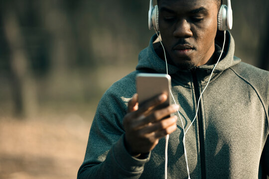Young adult man focused on smartphone with headphones in park - Powered by Adobe