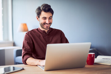 Cheerful man laughing while working on laptop from home