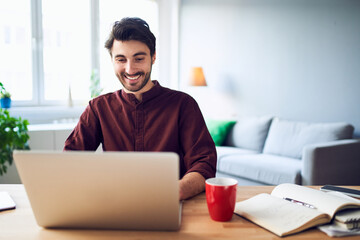Smiling young freelancer working from home using laptop
