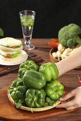 Fresh Green Bell Peppers in Basket with Healthy Vegetables on Wooden Kitchen Table