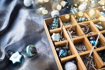 A box with vintage Christmas ornaments is showcased on a silver fabric backdrop, creating a festive display