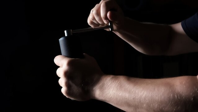 A man grinding beans using a hand coffee grinder. Milling handle process close-up on black background side view. Working male hands. Preparing drink. - Powered by Adobe