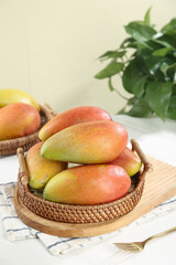 Fresh Ripe Mangoes in Wicker Basket on Kitchen Table with Green Plant