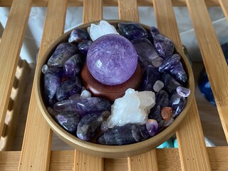 Amethyst crystal sphere displayed in a bowl of mixed stones for spiritual and healing decor
