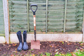 A pair of wellington boots and a shovel in the garden in landscape orientation, gardening hobby concept