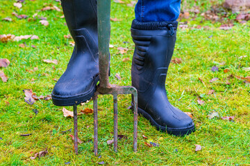 Person in wellington boots with foot on a gardening fork on the grass lawn