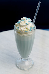 Blue milkshake in a tall glass with a cap of whipped cream