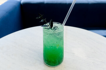 Bright green cocktail with ice and dark garnish in a glass on the table.