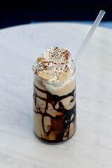 Iced coffee with chocolate syrup, whipped cream and peanuts on a white table