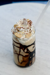 Iced coffee with chocolate syrup, whipped cream and peanuts on a white table