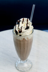 Chocolate milkshake with whipped cream and cocoa chips in a tall glass.