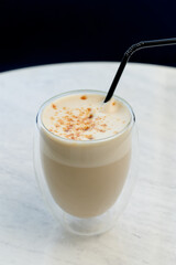 Hot milky coffee drink with foam and brown sprinkles with a black straw.