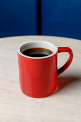 A red ceramic mug with black coffee stands on a white marble table